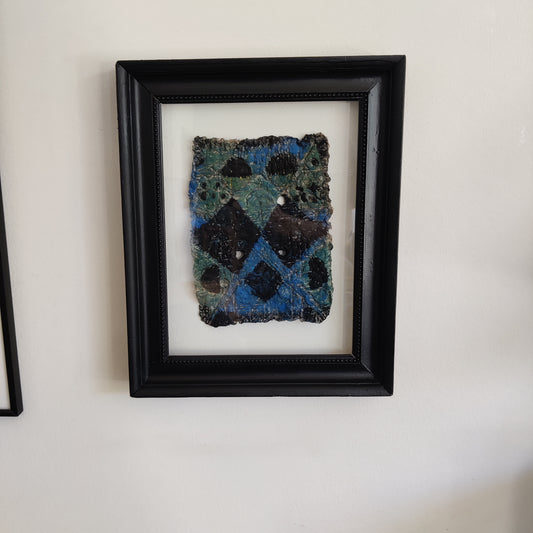 Framed paper pulp piece with blue and black pattern on a white wall