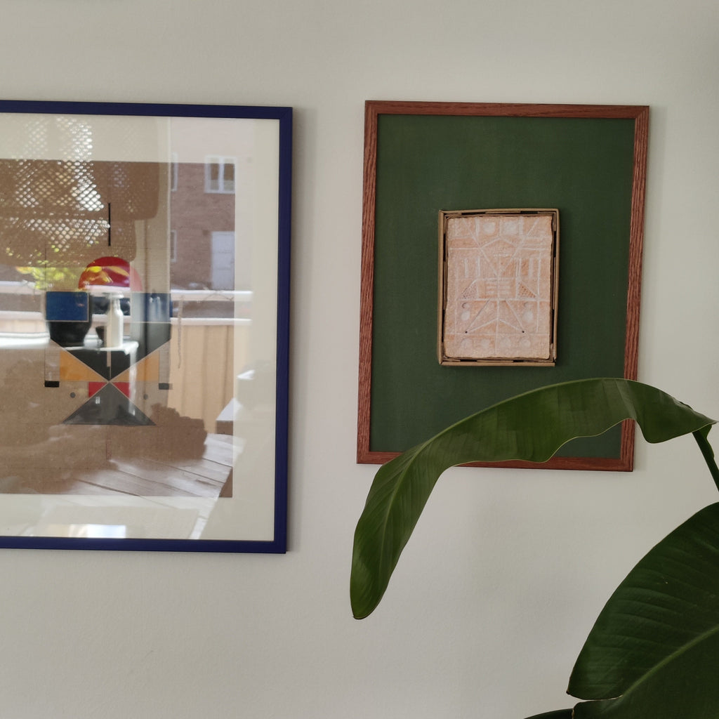 Two framed artworks on a wall with a plant in the foreground